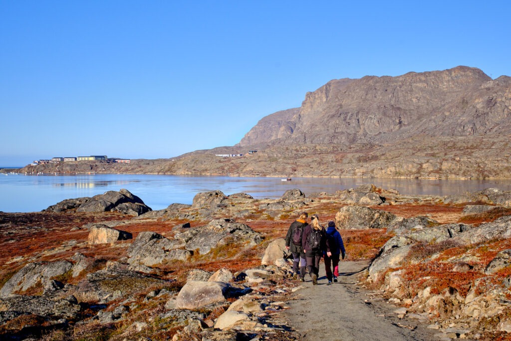 Three people walking along a rocky coastal path near Sisimiut, Greenland