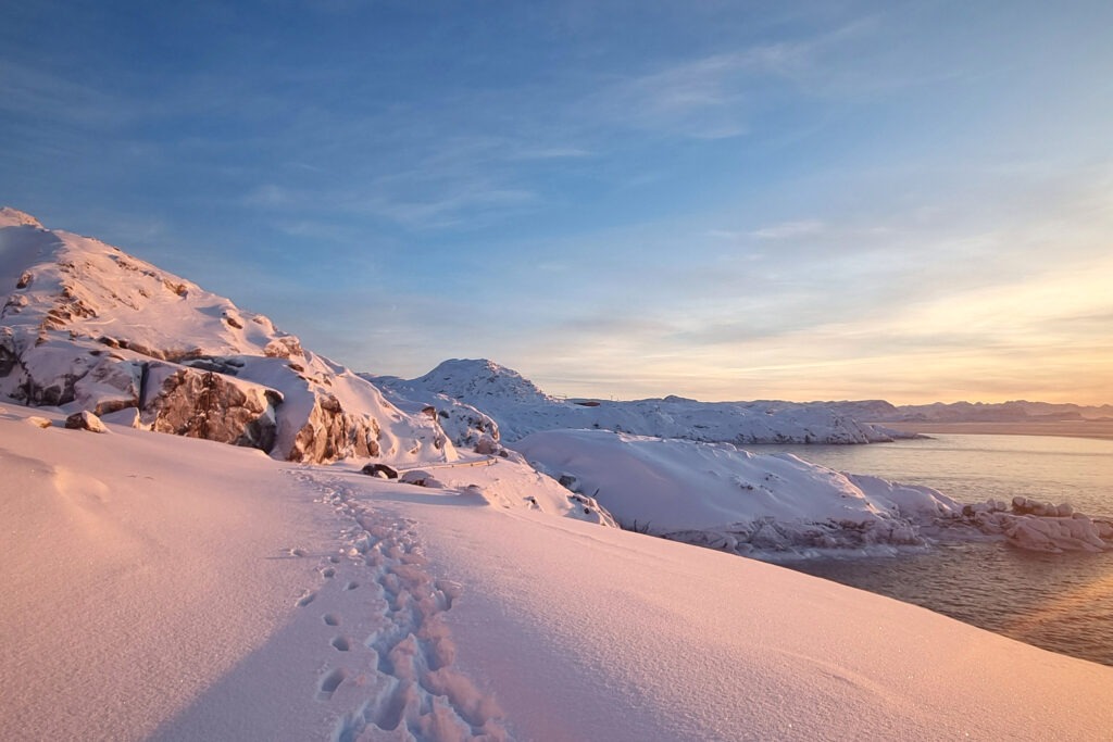 Footprints in fresh snow along a coastal path in Greenland in winter light