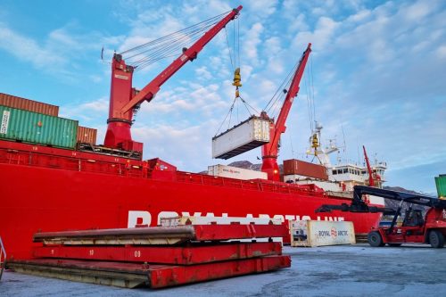 Royal Arctic Line cargo ship docked at a harbor with cranes and industrial equipment.