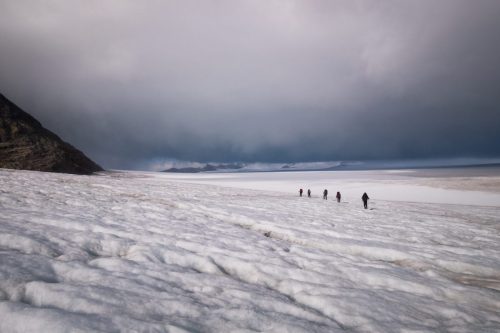 Small group of people walking across a glacier in Argentina beneath heavy cloud cover.