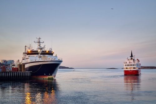 Two ships floating on calm water at dusk with soft light reflecting on the sea