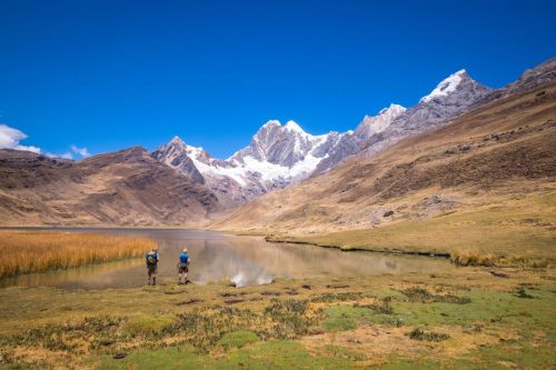 Hikers walking through a high mountain valley in Peru with snow-covered peaks under a clear sky.