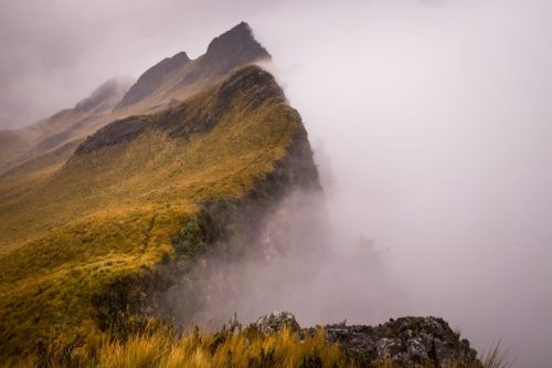 Fog rolling over a steep green ridge in Ecuador, partially obscuring the landscape.