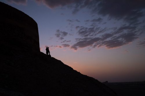 Silhouette of a person standing on a hillside at dusk in Iran, with fading light in the sky.