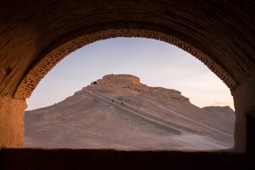 View through a stone arch framing a desert hill in Iran under soft evening light.