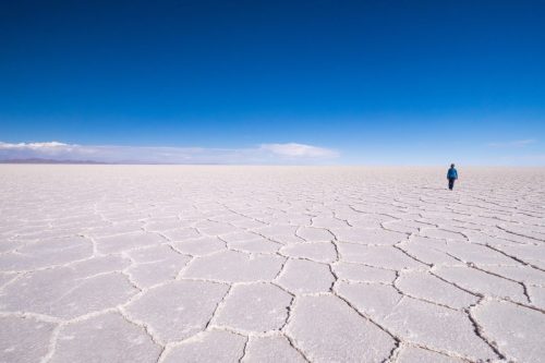 Solitary figure walking across a vast salt flat in Bolivia under a deep blue sky.